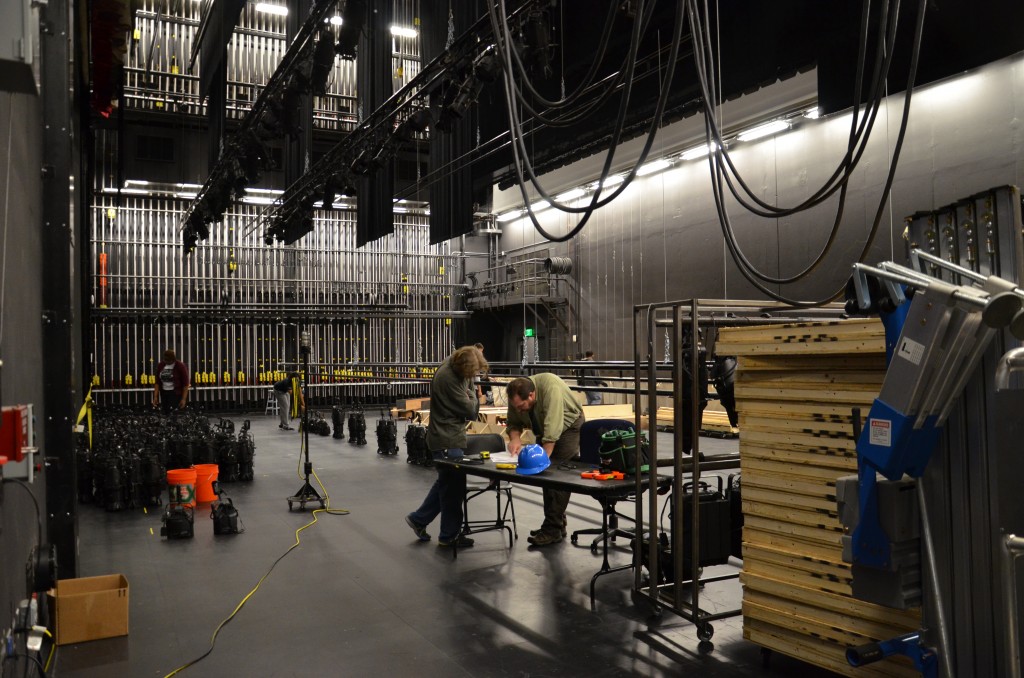 Students work at a table on the Proscenium Theatre stage, surrounded by wooden pallets and lights