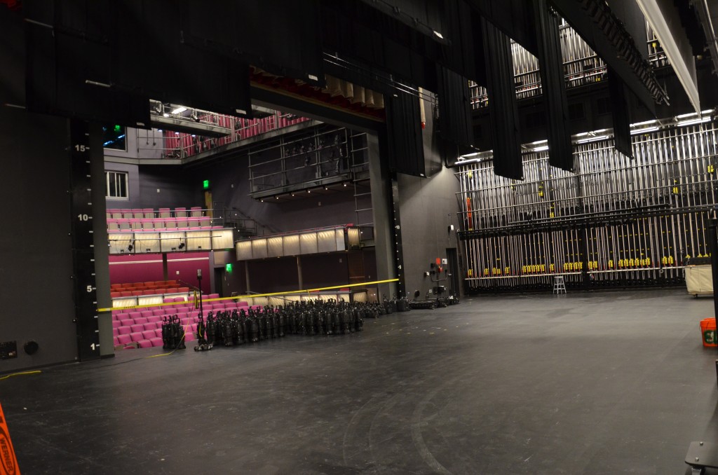 Empty Proscenium theatre stage. Rows of lights are lined up on the downstage apron.