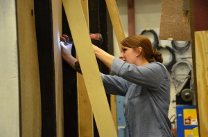 A student drills a screw into a tall, vertical piece of plywood.