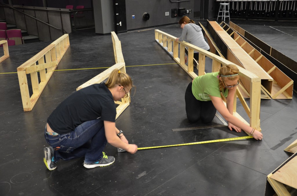 Two students use a tape measure on the Proscenium Theatre floor